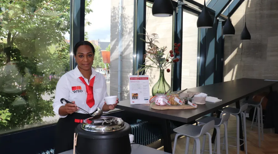 Vrouw van de catering kijkt lachend de camera in voordat ze soep inschenkt