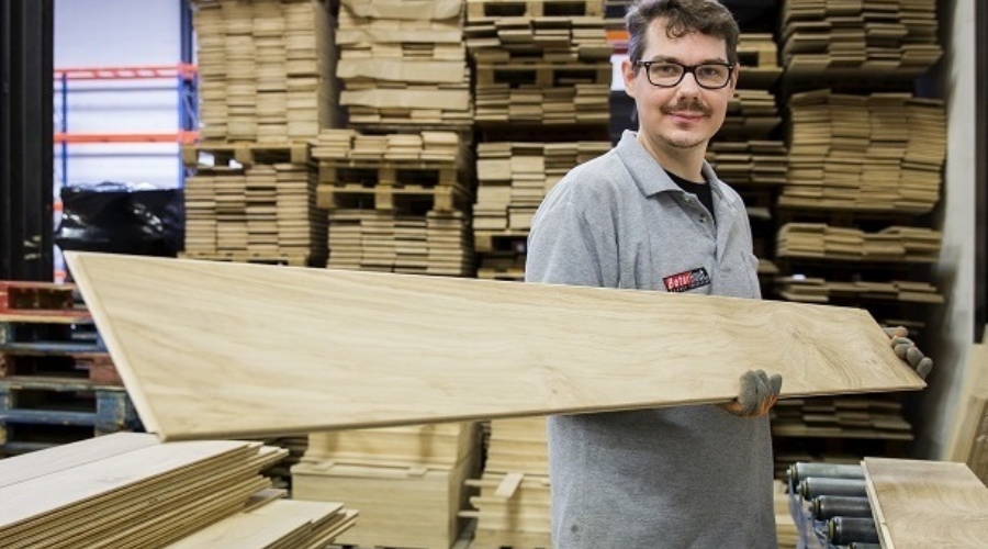 Een medewerker in de houtwerkplaats heeft een houten plank in zijn handen