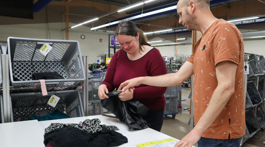 Een medewerker krijgt uitleg van de werkbegeleider in het textiel sorteer centrum