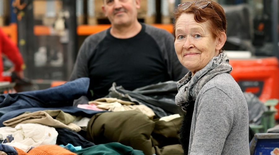 Vrouw kijkt lachend de camera in en is aan het werk in textielsorteercentrum Schijndel